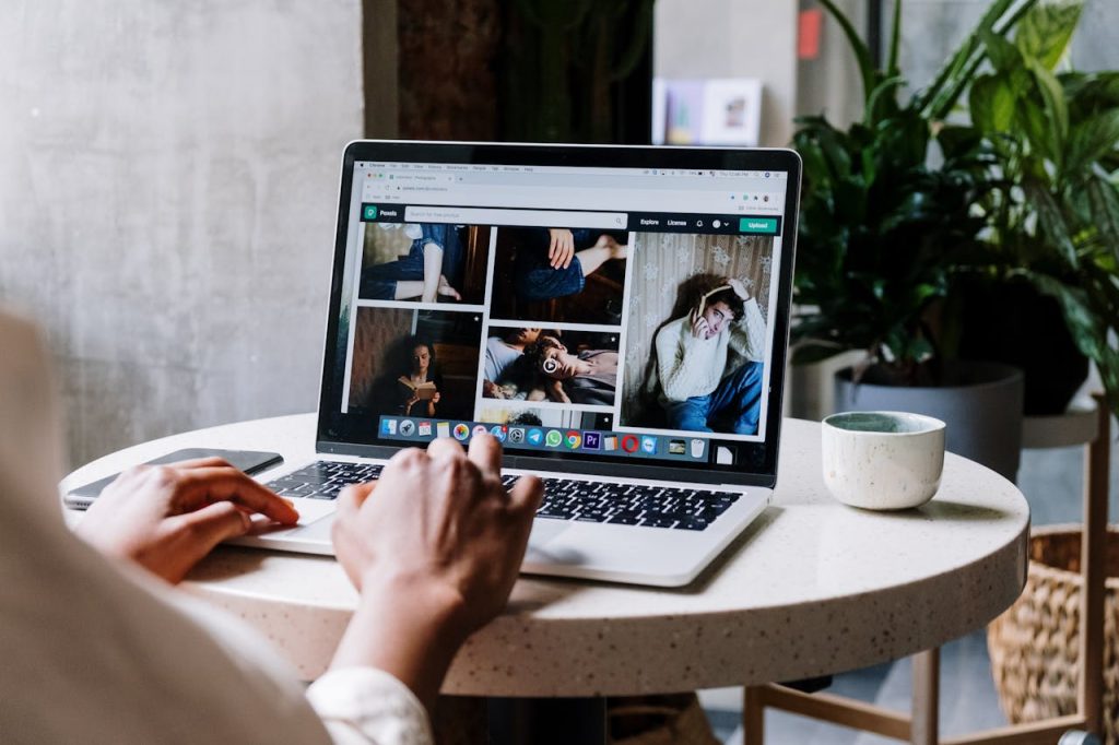 A person browsing photos on a laptop at a round table with a mug and plants inside.